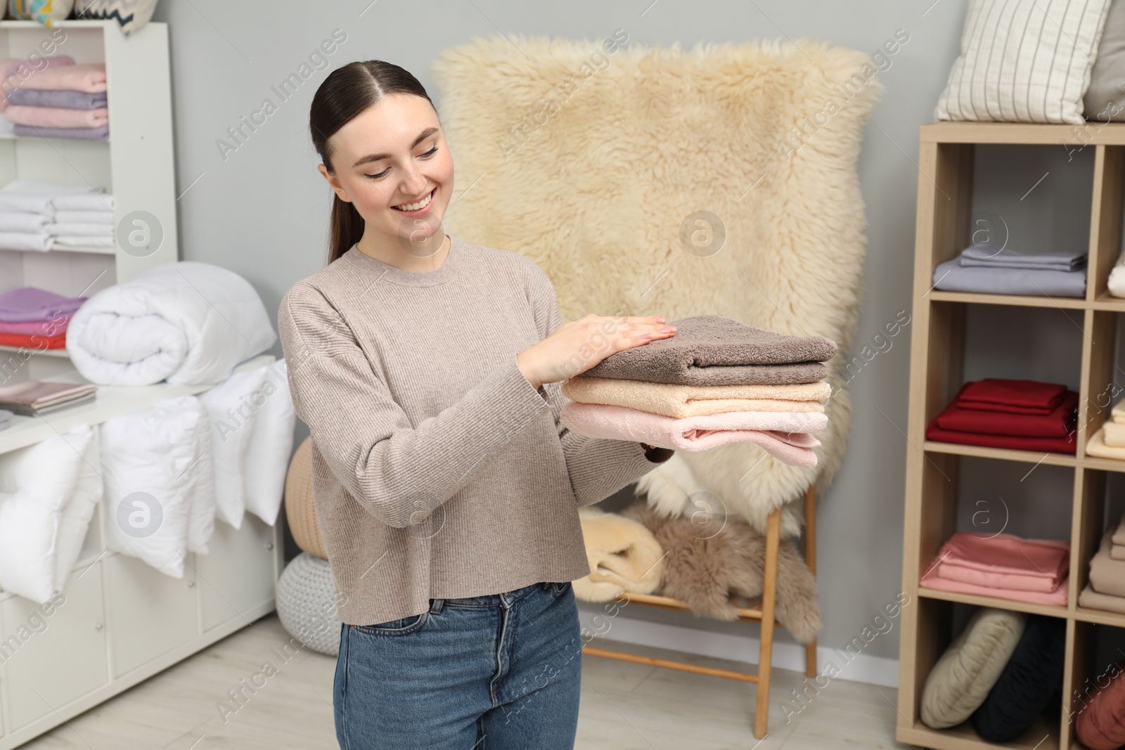 Photo of Smiling young woman holding stack of towels in home textiles store