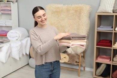 Smiling young woman holding stack of towels in home textiles store
