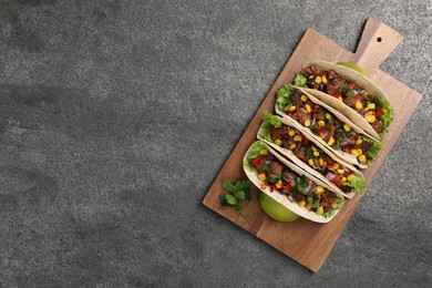 Photo of Delicious tacos with meat and vegetables on gray textured table, top view. Space for text