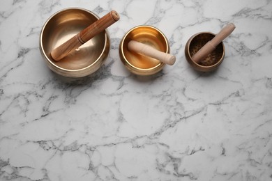 Golden singing bowls with mallets on white marble table, flat lay. Space for text