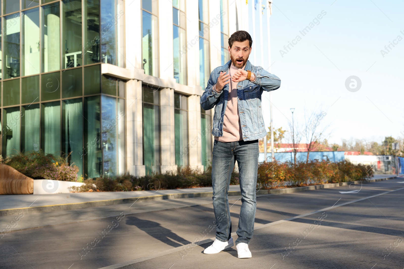 Photo of Emotional man checking time on watch near building. Being late concept