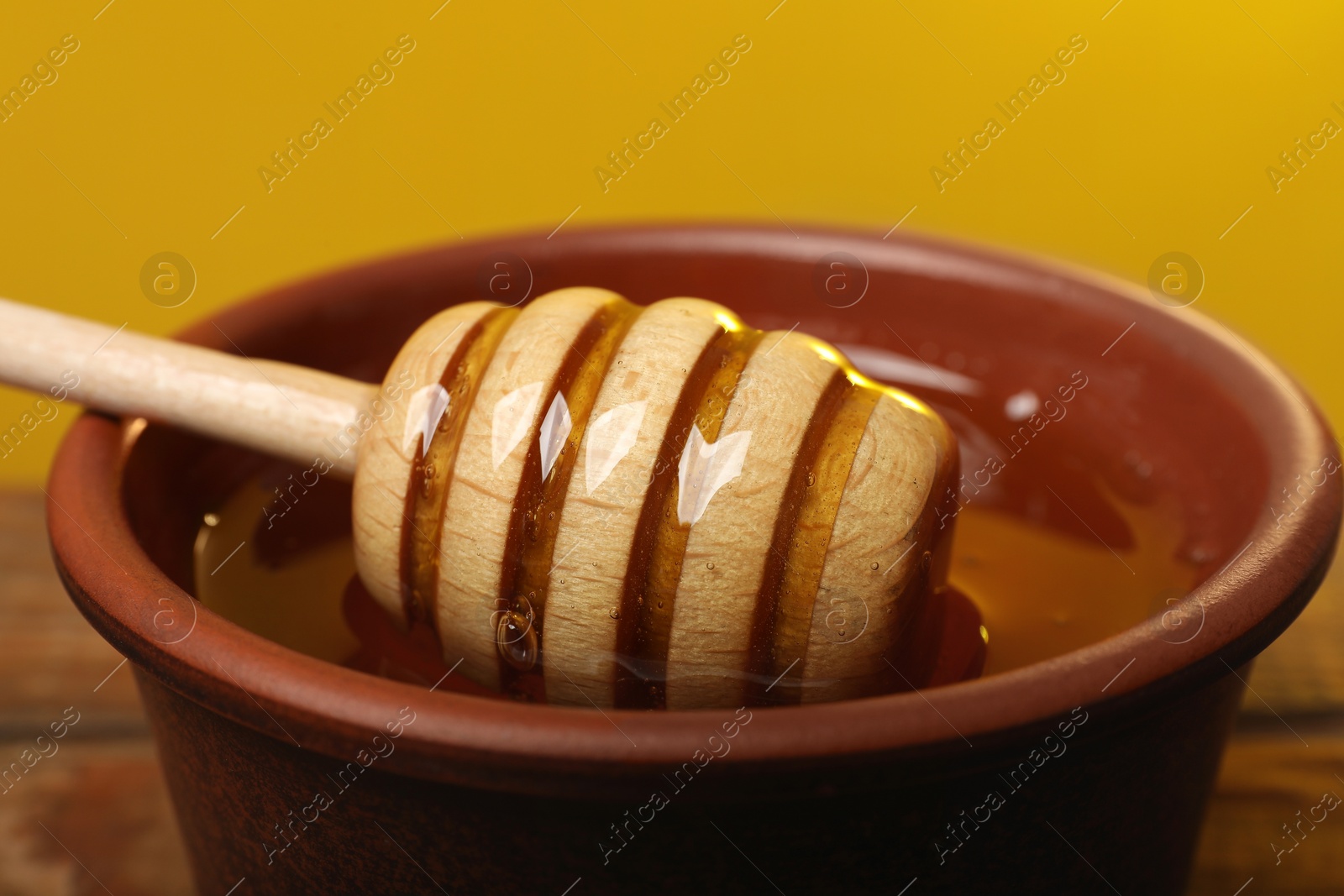 Photo of Dipper with honey in bowl on table against golden background, closeup