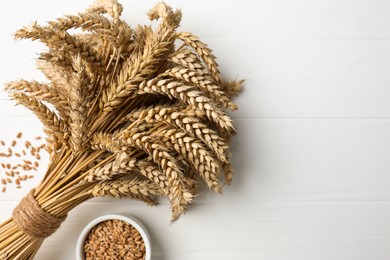 Bunch of wheat and grains on white wooden table, flat lay. Space for text