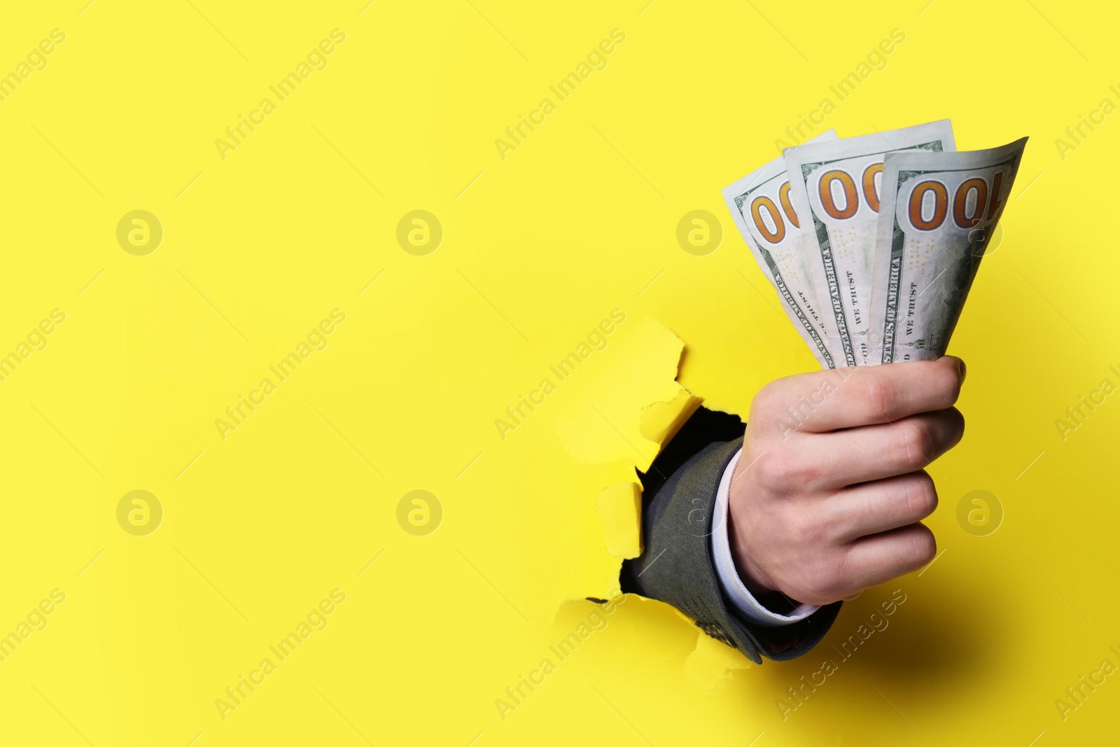 Photo of Businessman breaking through yellow paper with money in fist, closeup. Space for text