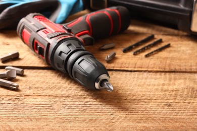 Photo of Electric screwdriver with bits and drills on wooden table, closeup