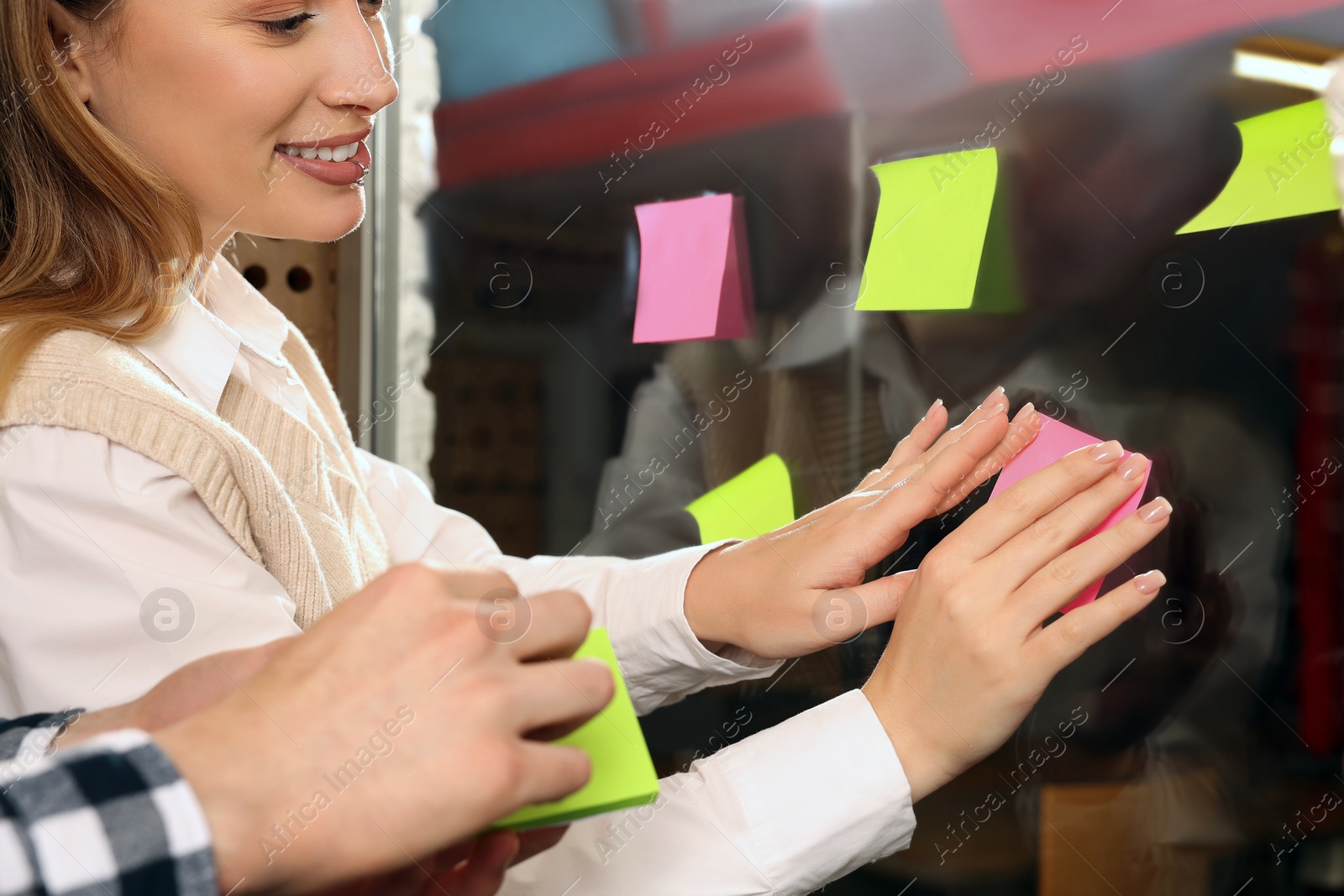Photo of Employees putting colorful sticky notes on glass door in office. Team work motivation