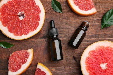 Flat lay composition with grapefruit slices and bottles of essential oil on wooden background