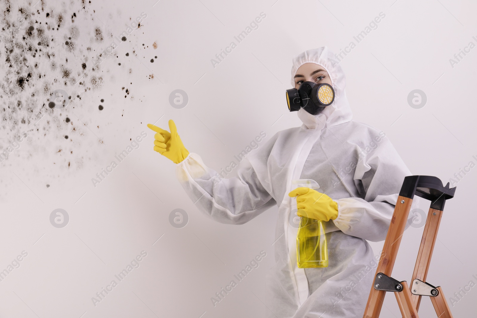 Image of Woman in protective suit with mold remover pointing at affected wall