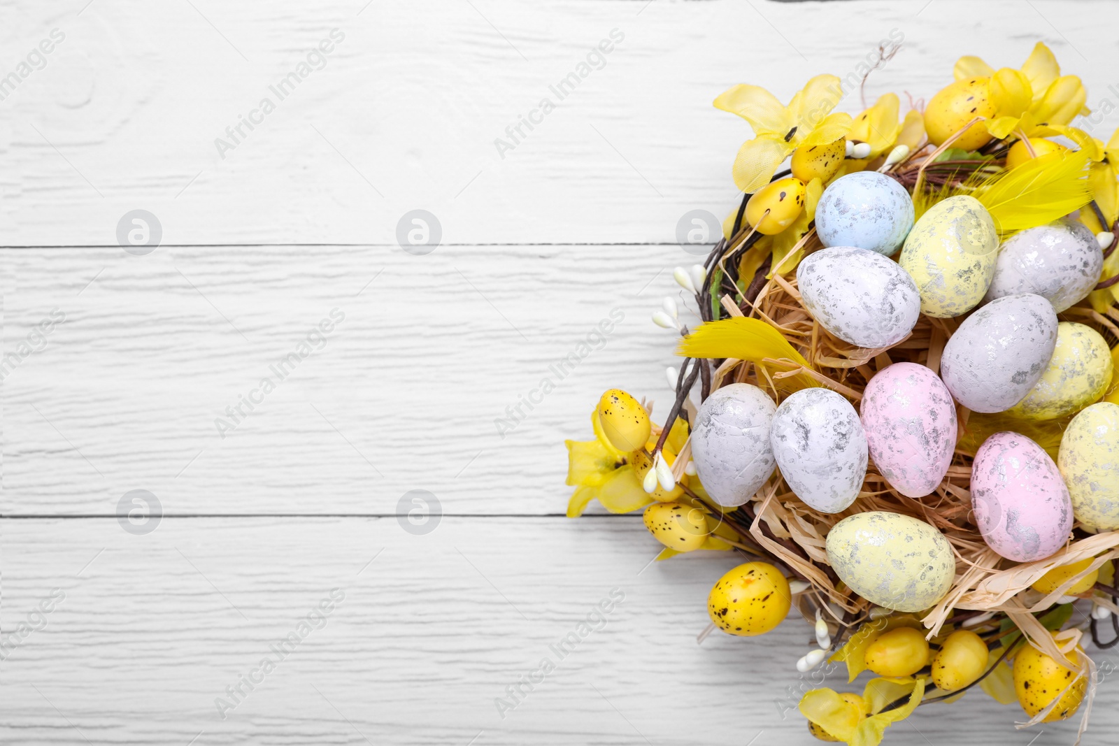 Photo of Festively decorated Easter eggs on white wooden table, top view. Space for text