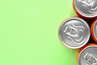 Photo of Energy drink in cans on light green background, top view. Space for text