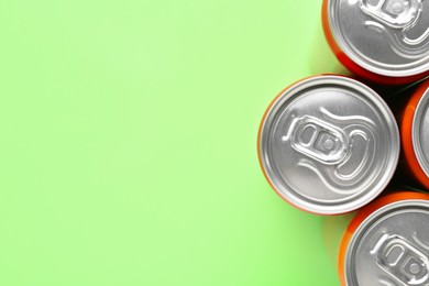 Energy drink in cans on light green background, top view. Space for text