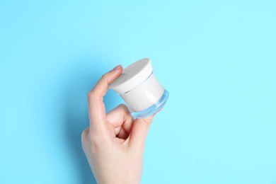 Photo of Woman holding jar of cream on light blue background, closeup