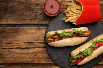 Tasty hot dogs, French fries and sauce on wooden table, flat lay with space for text. Fast food