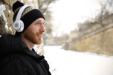 Young man listening to music with headphones near stone wall. Space for text