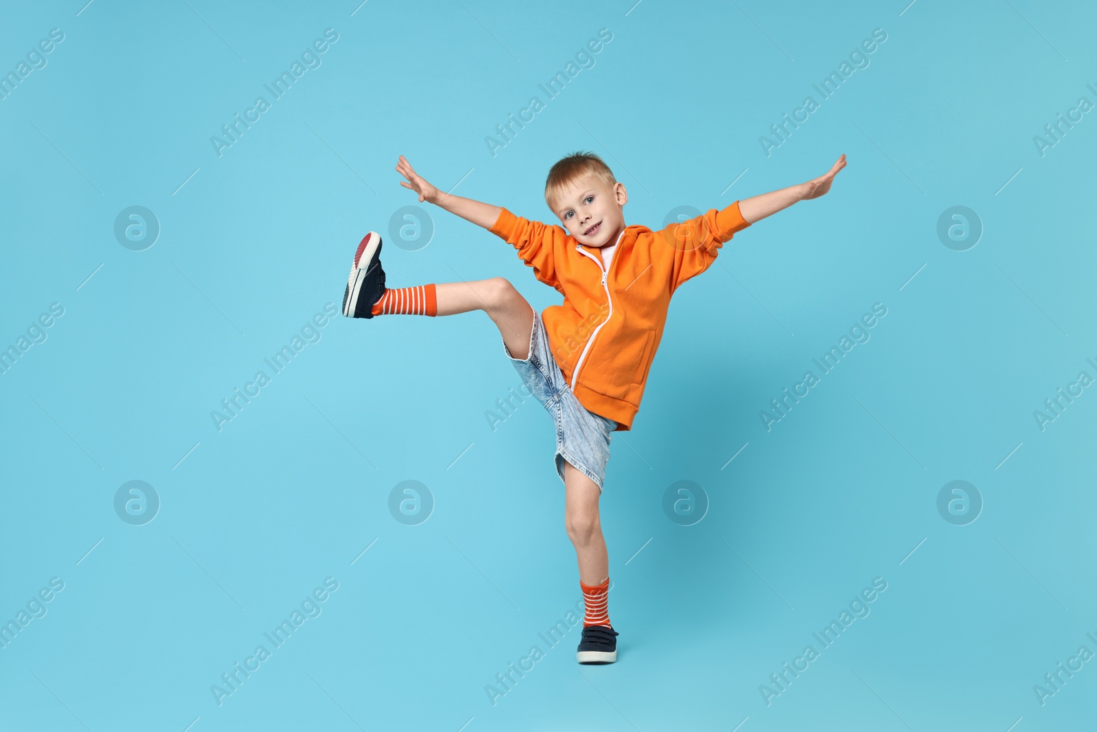 Photo of Happy little boy dancing on light blue background