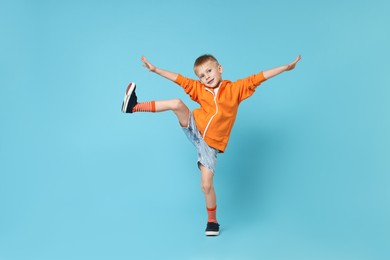 Happy little boy dancing on light blue background