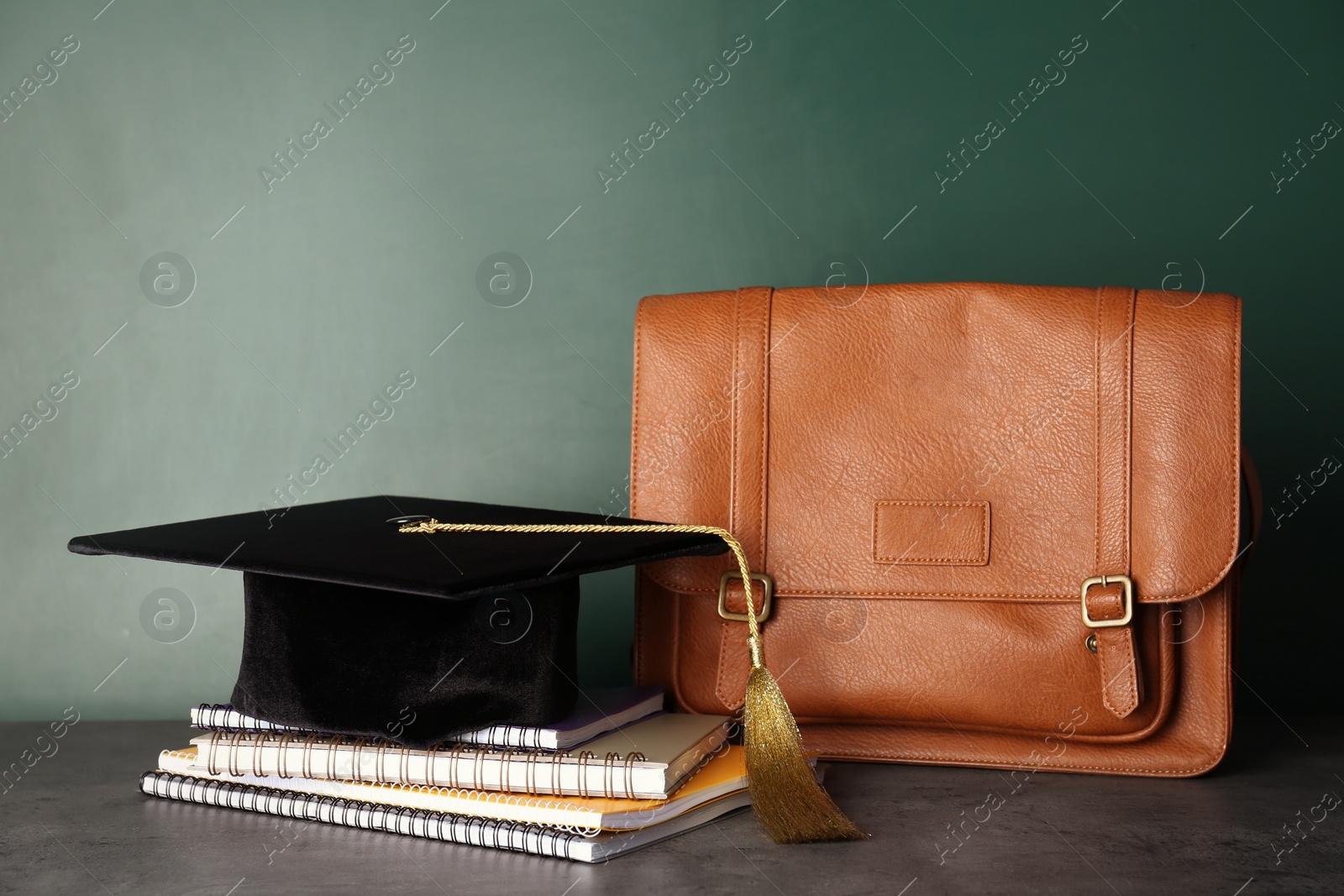 Photo of Graduation hat with notebooks and briefcase on table near chalkboard