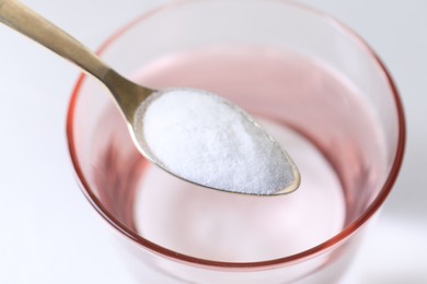 Spoon with baking soda over glass of water on white background, closeup