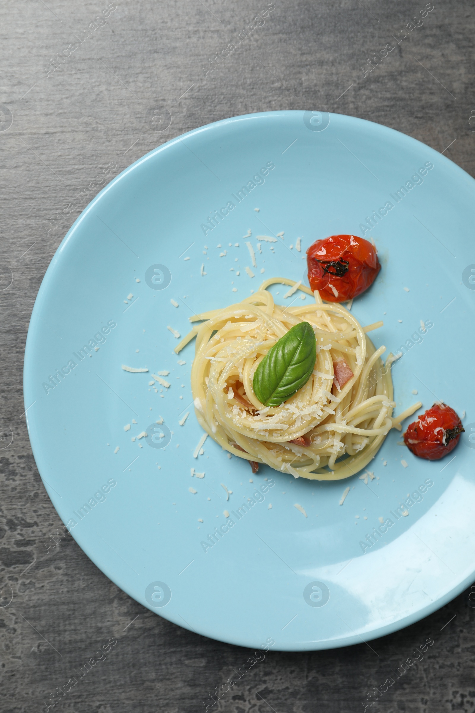 Photo of Tasty spaghetti with tomatoes and cheese on grey table, top view. Exquisite presentation of pasta dish