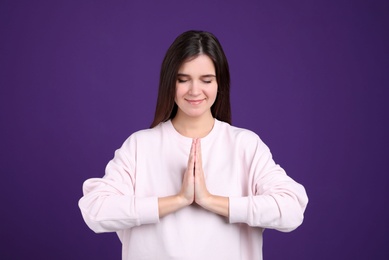 Photo of Young woman meditating on purple background. Stress relief exercise