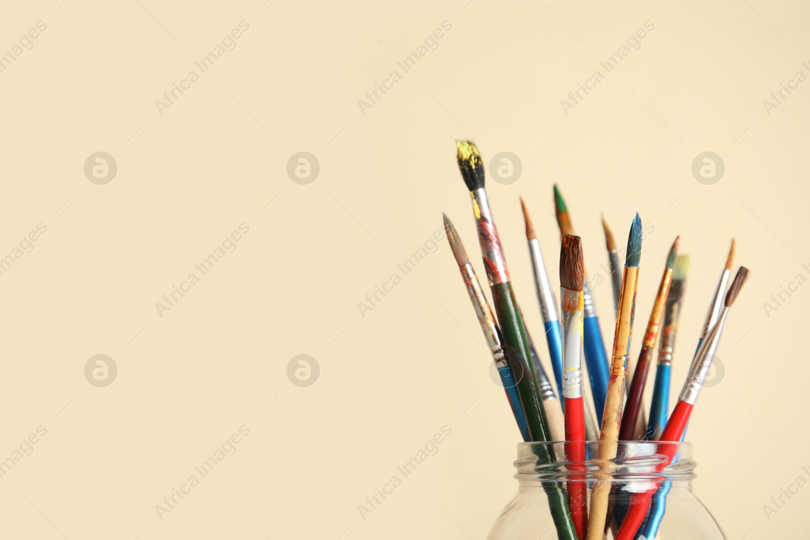 Photo of Glass with paint brushes on color background. Space for text