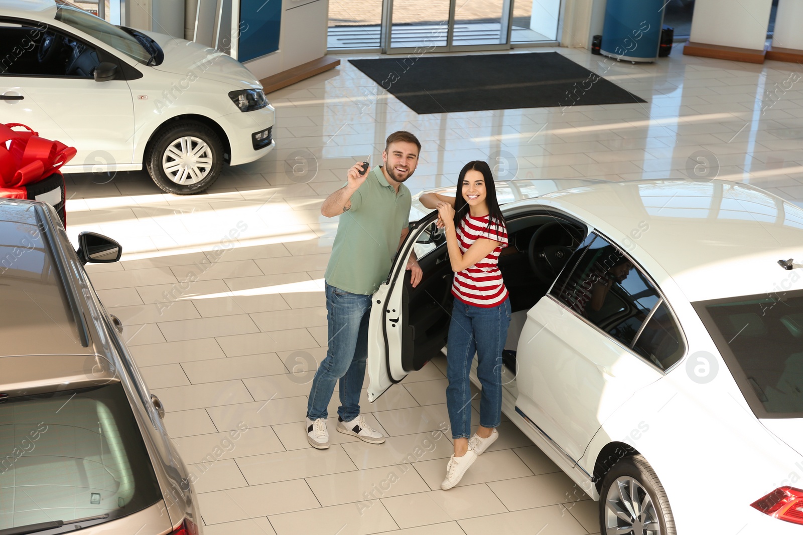 Photo of Happy couple with car key in modern auto dealership