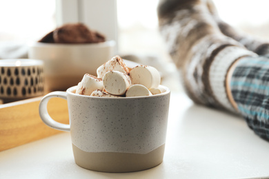 Photo of Cup of delicious hot cocoa with marshmallows near window indoors. Winter drink