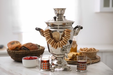 Traditional Russian samovar with treats on white table in kitchen