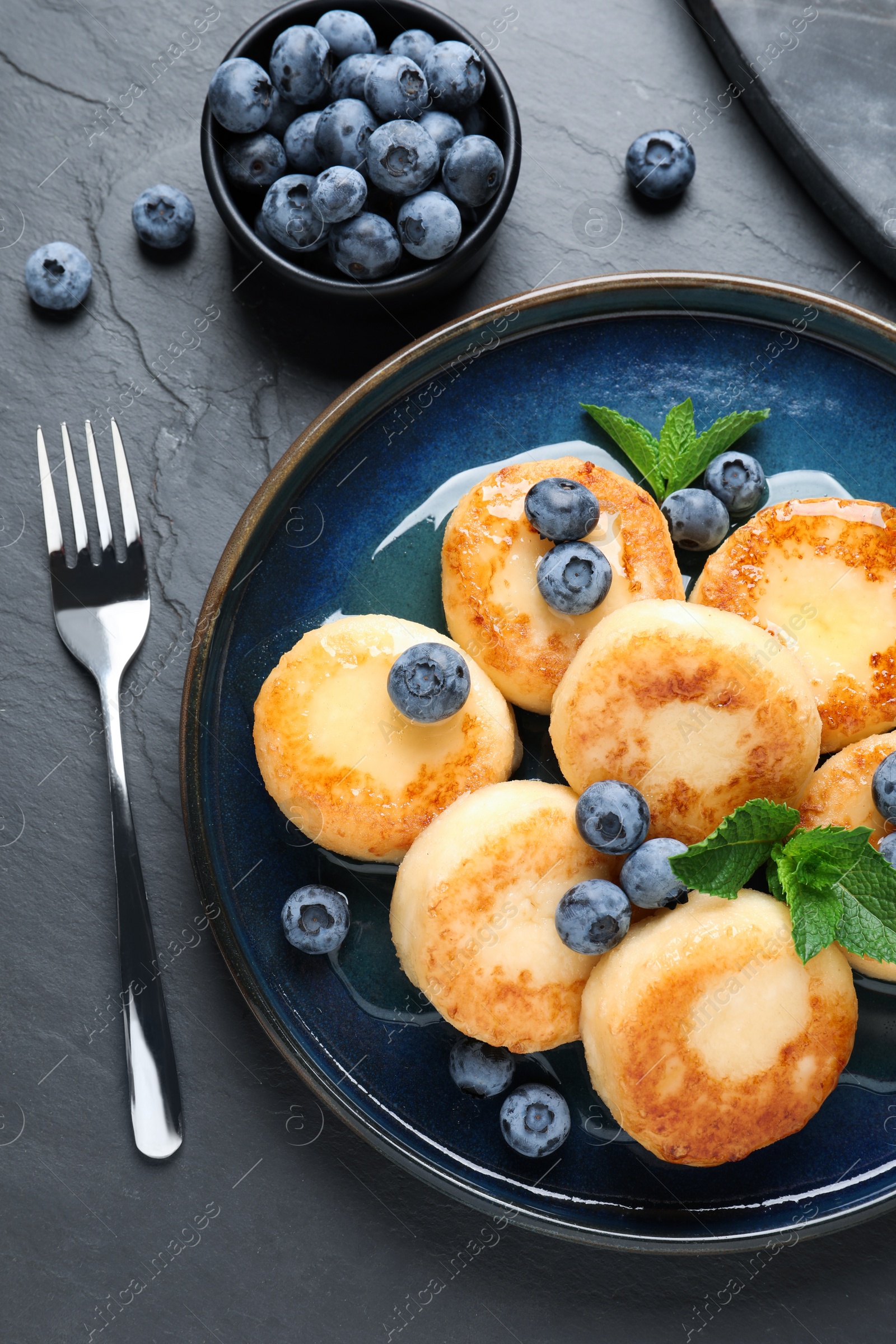 Photo of Delicious cottage cheese pancakes with blueberries on black table, flat lay