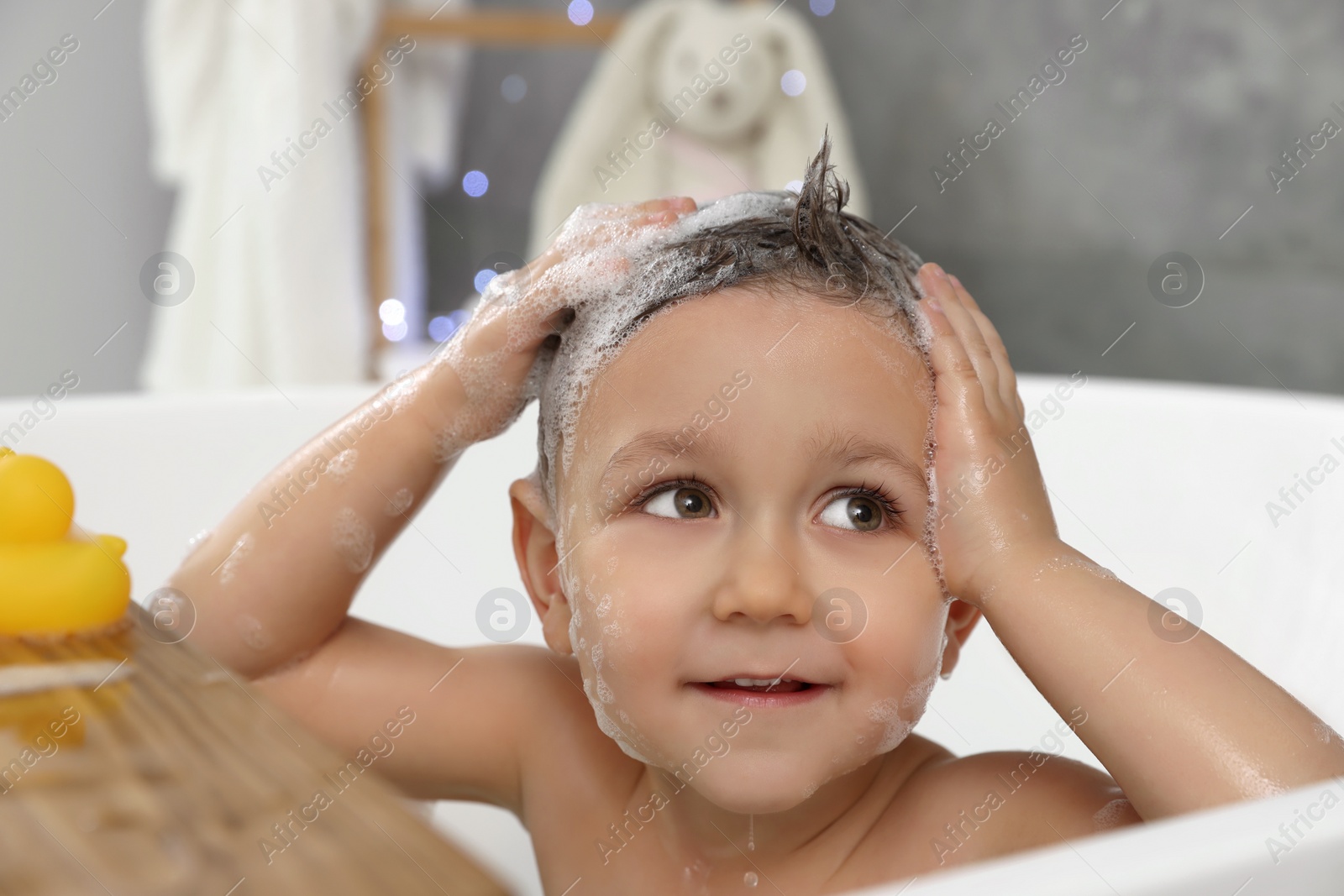 Photo of Cute little boy washing hair with shampoo in bathroom