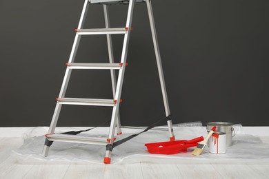 Photo of Metallic folding ladder and painting tools near gray wall indoors
