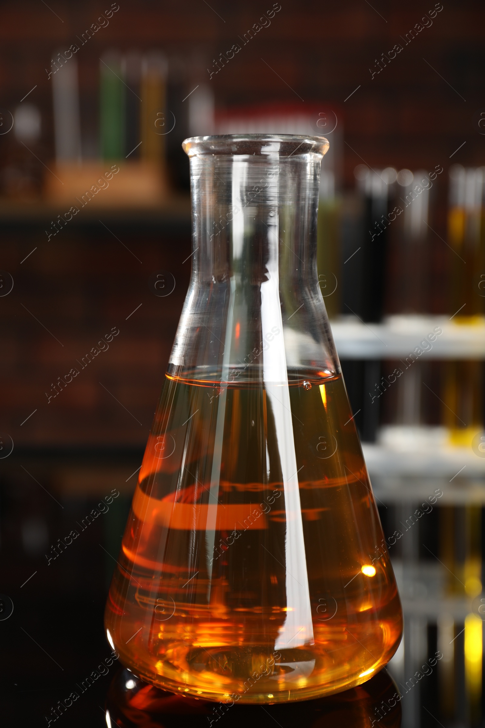 Photo of Flask with yellow oil on black mirror table, closeup