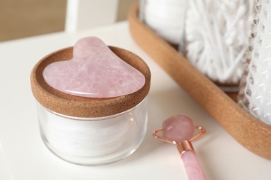 Photo of Rose quartz gua sha tool, natural face roller and toiletries on white shelf, closeup
