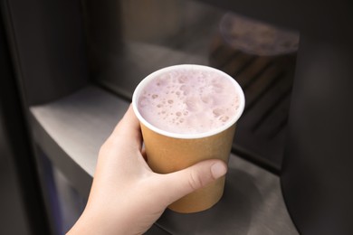 Photo of Girl holding paper cup with hot drink near coffee vending machine, closeup