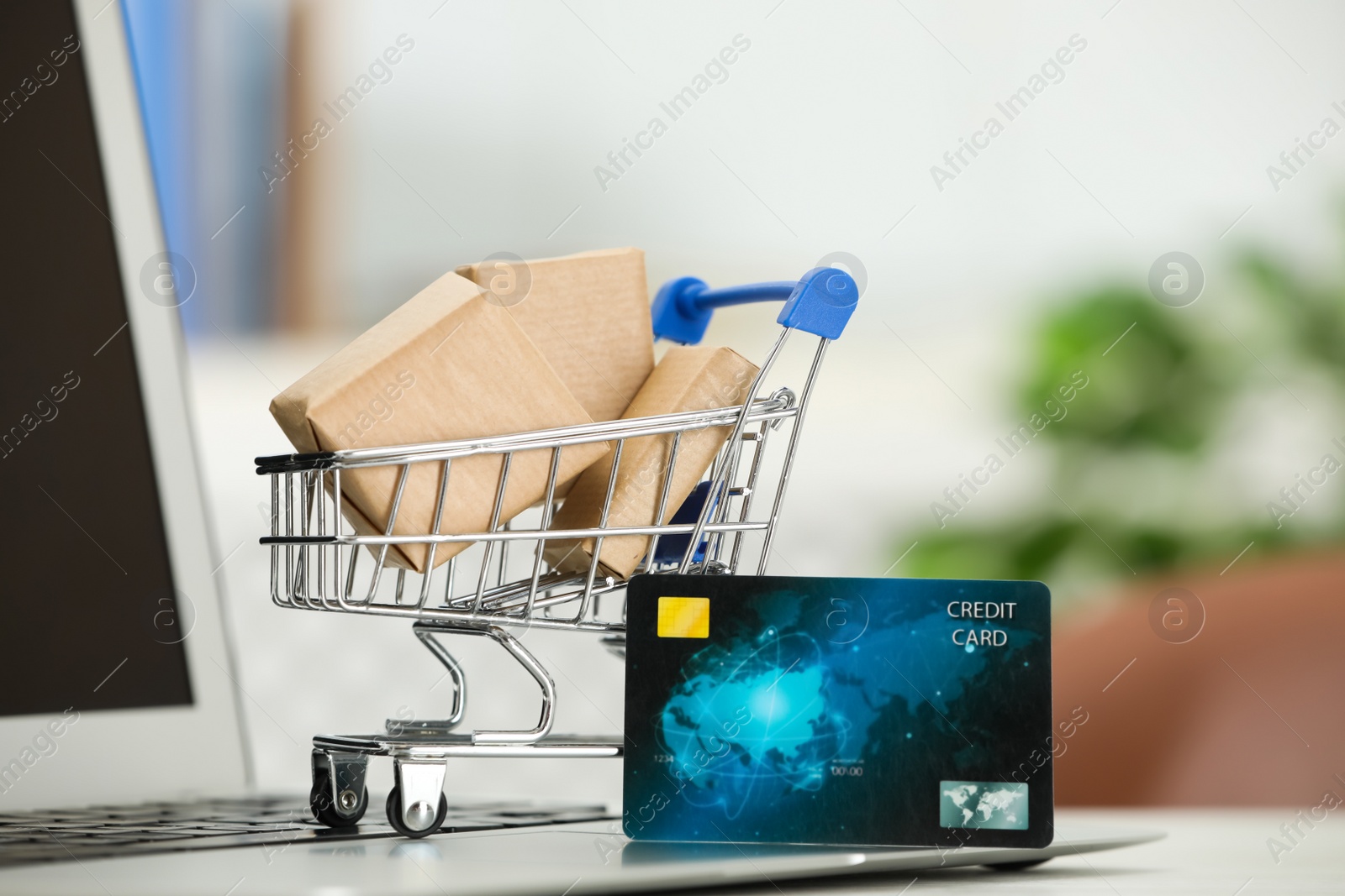 Photo of Online payment concept. Small shopping cart with bank card, boxes and laptop on table