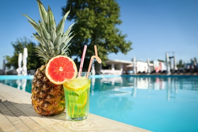 Photo of Tasty refreshing cocktail and pineapple on edge of swimming pool. Party items