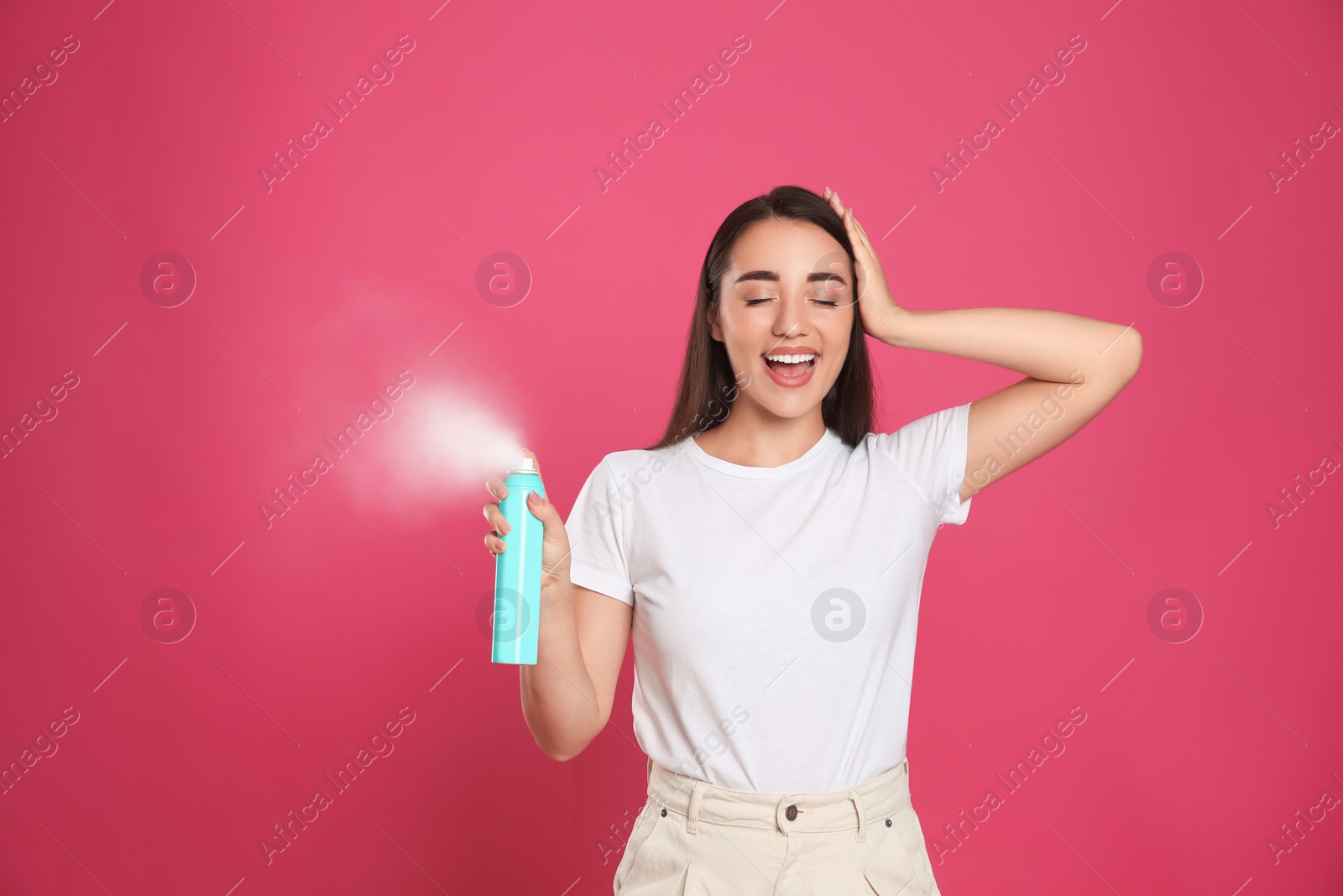 Photo of Young woman applying dry shampoo against pink background