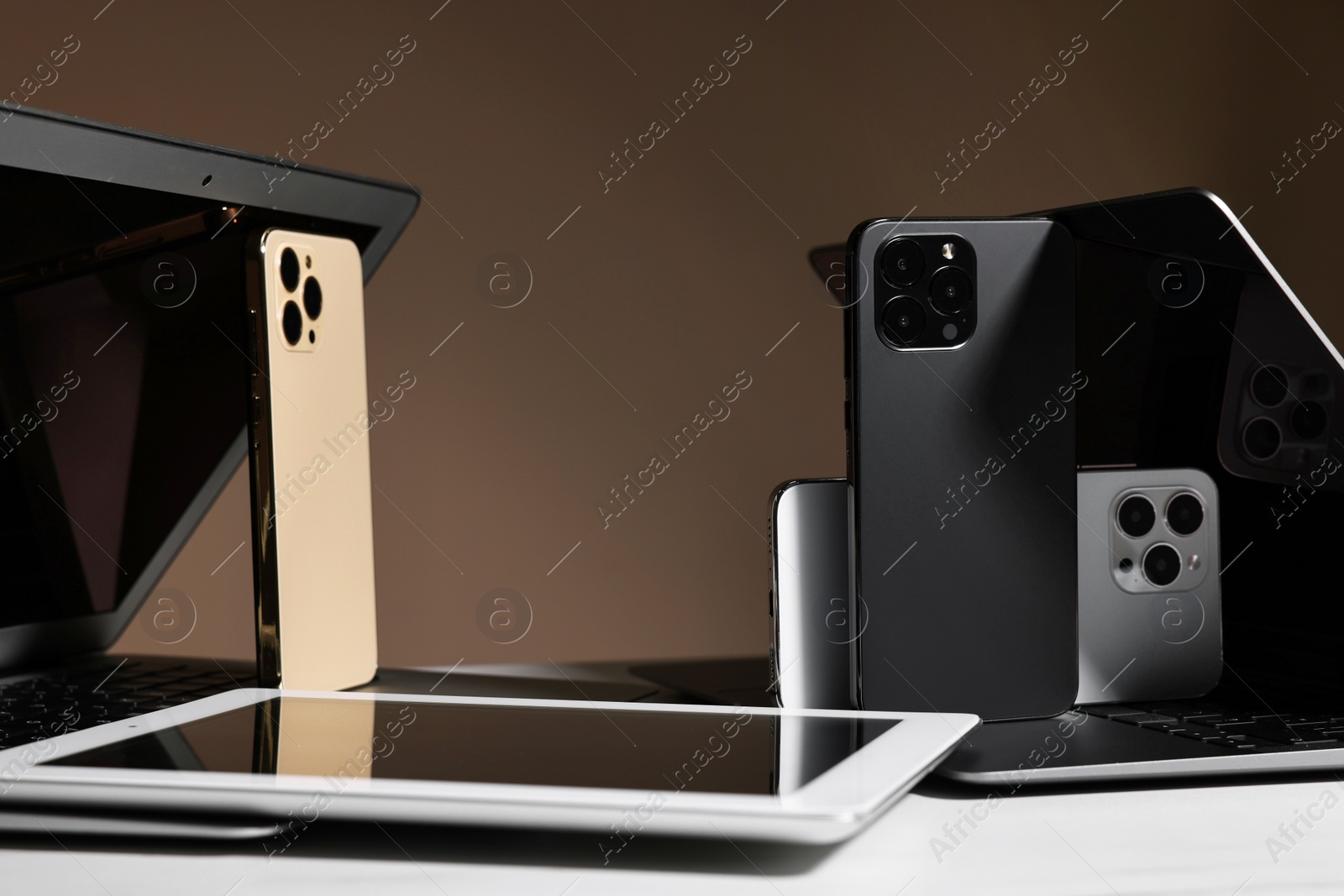 Photo of Many different modern gadgets on white table against brown background, closeup