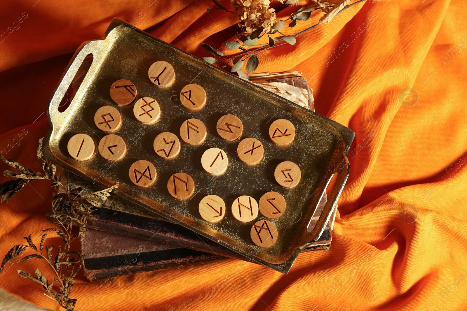 Photo of Tray with wooden runes, dried plants and old books on orange fabric, flat lay