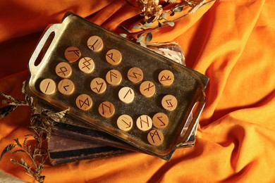 Photo of Tray with wooden runes, dried plants and old books on orange fabric, flat lay