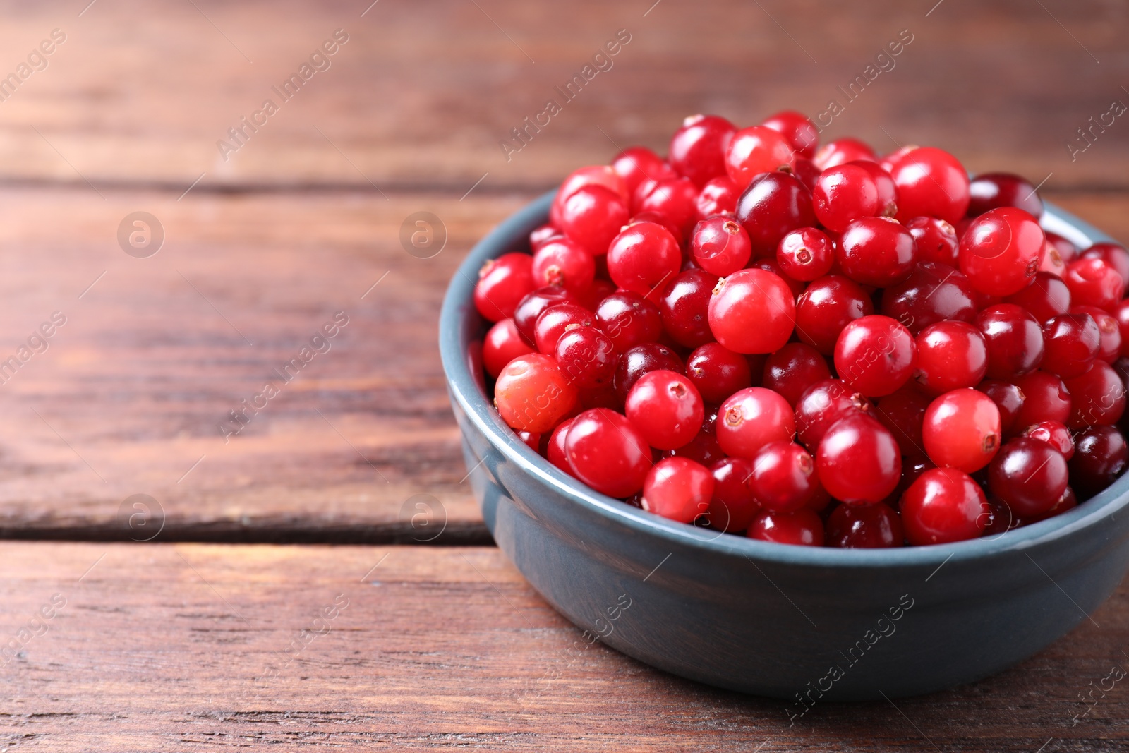 Photo of Fresh ripe cranberries in bowl on wooden table, closeup. Space for text