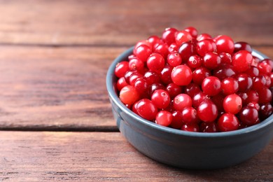 Photo of Fresh ripe cranberries in bowl on wooden table, closeup. Space for text