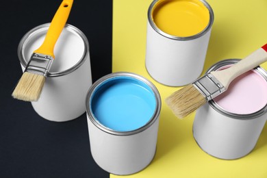 Photo of Cans of colorful paints and brushes on color background