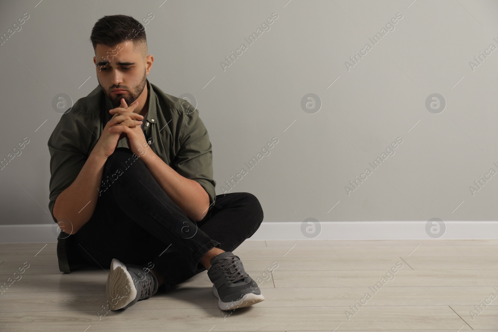 Photo of Sad man sitting on floor near light grey wall. Space for text