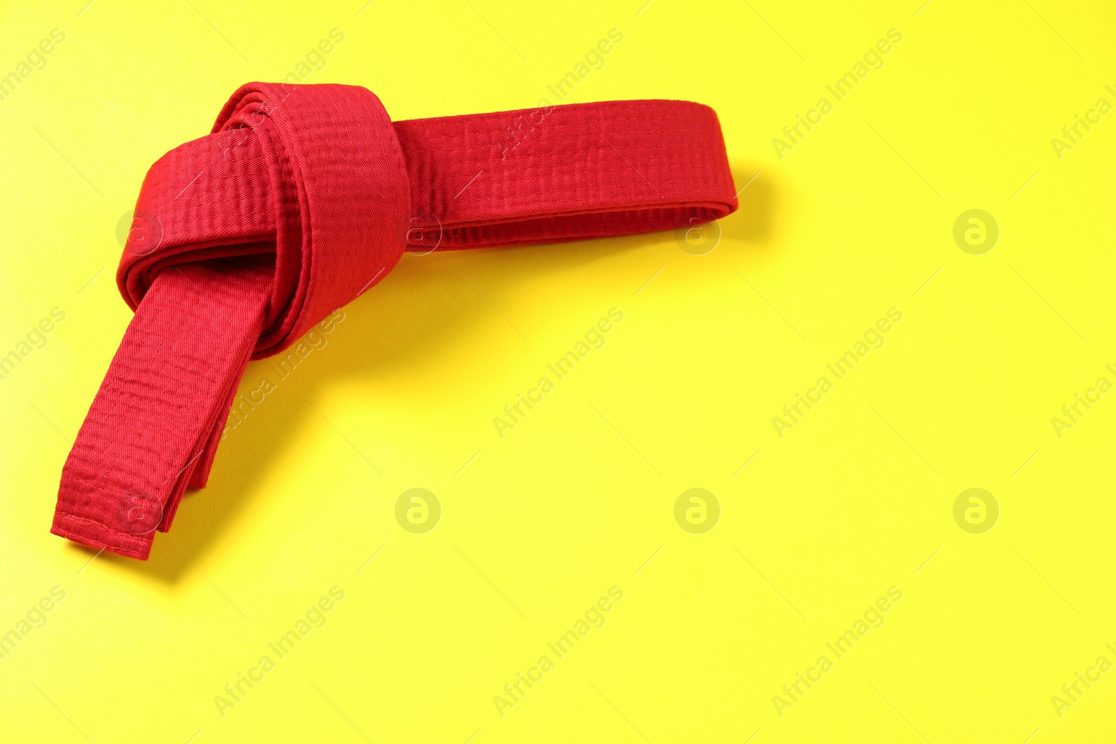 Photo of Red karate belt on yellow background, top view. Space for text