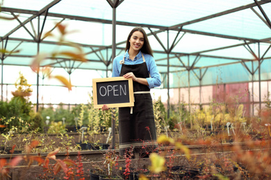 Female business owner holding OPEN sign in greenhouse