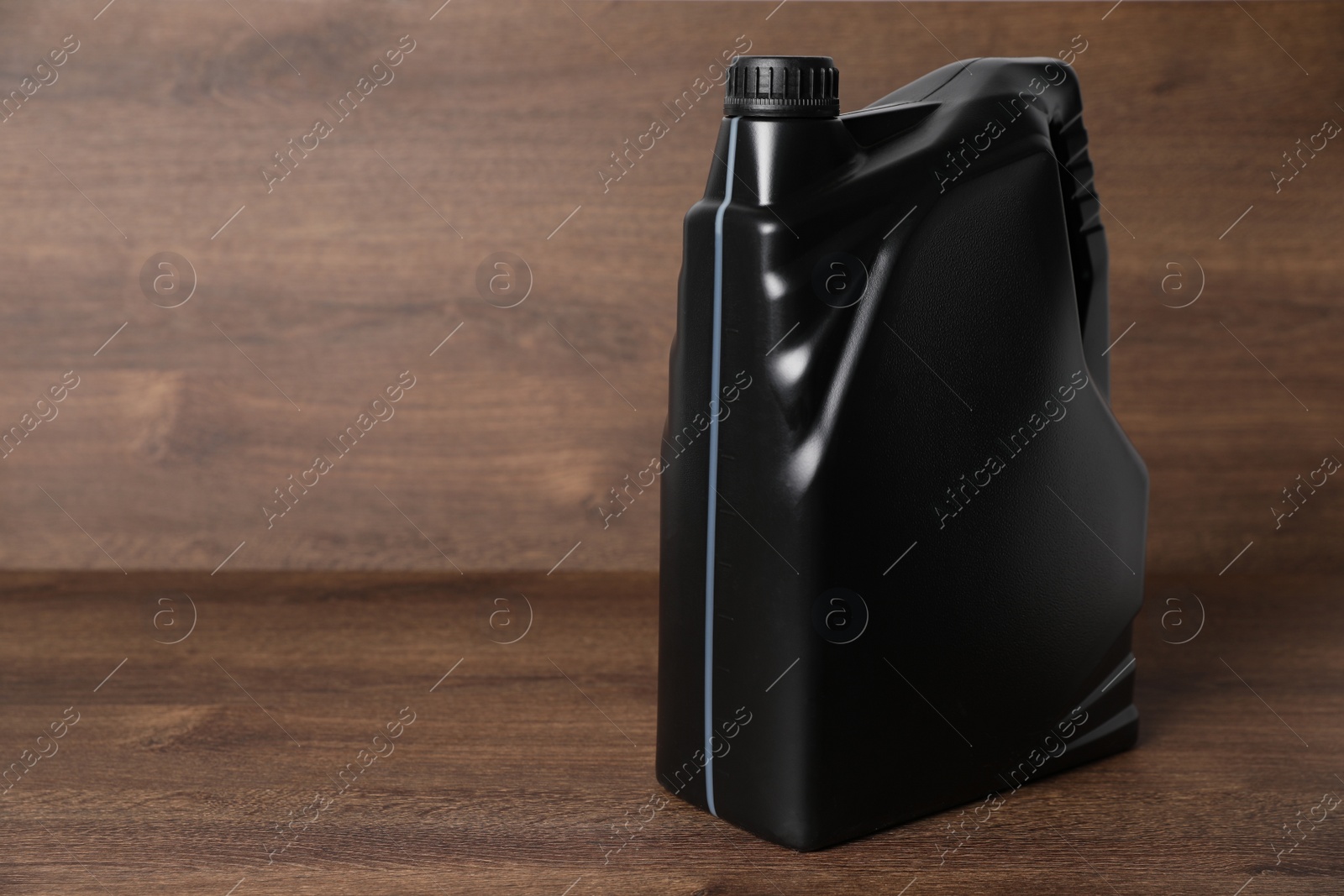 Photo of Motor oil in black canister on wooden background, space for text