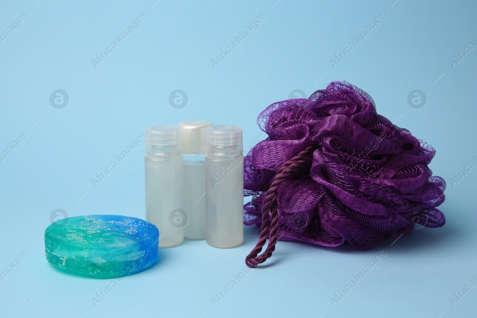 Photo of Purple shower puff and cosmetic products on light blue background