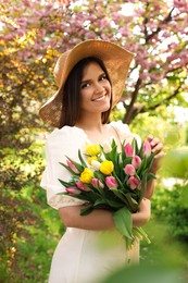Beautiful young woman with bouquet of tulips in park on sunny day