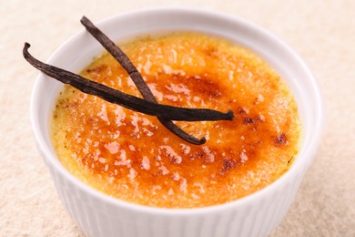Photo of Delicious creme brulee and vanilla pods in bowl on light textured table, closeup